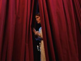 Un'attrice di uno spettacolo teatrale scosta la tenda per guardare il pubblico in sala