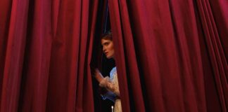 Un'attrice di uno spettacolo teatrale scosta la tenda per guardare il pubblico in sala