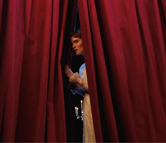 Un'attrice di uno spettacolo teatrale scosta la tenda per guardare il pubblico in sala