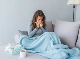 Ragazza influenzata seduta sul divano con la coperta e la tisana