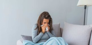 Ragazza influenzata seduta sul divano con la coperta e la tisana