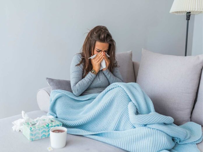 Ragazza influenzata seduta sul divano con la coperta e la tisana