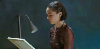 Rosa Ricci seduta sul letto guarda un quadro della madre